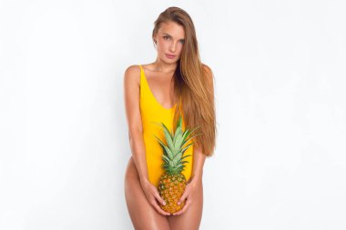Sarı mayo giymiş esmer, beyaz arka planda ananasla poz veren seksi esmer.