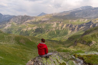 Taşların üzerindeki kırmızı ceketli genç adam Alplerin muhteşem manzarasına bakıyor.