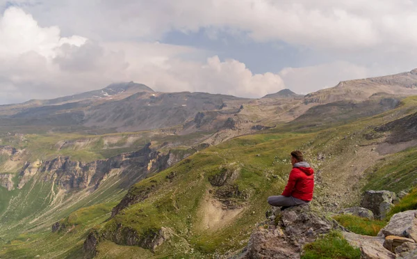 石の上に赤いジャケットを着た若い男がアルプスの山の壮大な景色を見ています — ストック写真
