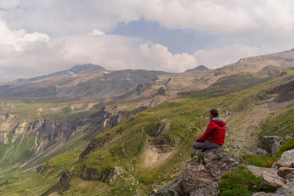石の上に赤いジャケットを着た若い男がアルプスの山の壮大な景色を見ています — ストック写真
