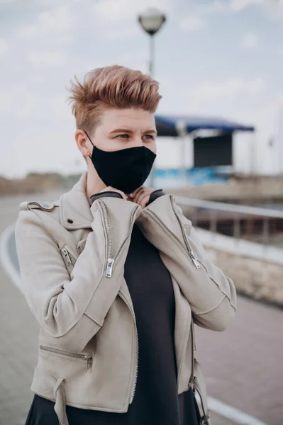 Siyah antiviral maskeli, kısa saçlı bir kız sokakta yürüyor.