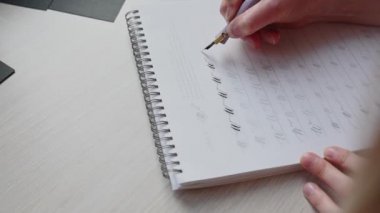 Bir kız kaligrafi defterini güzel sembollerle dolduruyor.