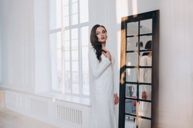 Beyaz parlak gelinlik içinde kahverengi saçlı güzel bir gelin fotoğraf stüdyosunda poz veriyor.