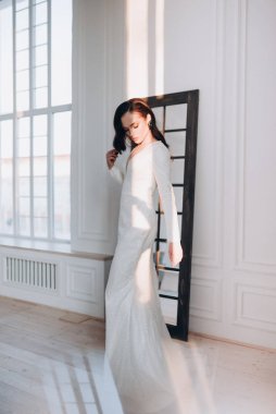 Beyaz parlak gelinlik içinde kahverengi saçlı güzel bir gelin fotoğraf stüdyosunda poz veriyor.