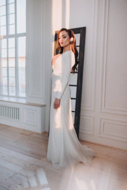 Beyaz parlak gelinlik içinde kahverengi saçlı güzel bir gelin fotoğraf stüdyosunda poz veriyor.