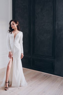 Beyaz parlak gelinlik içinde kahverengi saçlı güzel bir gelin fotoğraf stüdyosunda poz veriyor.