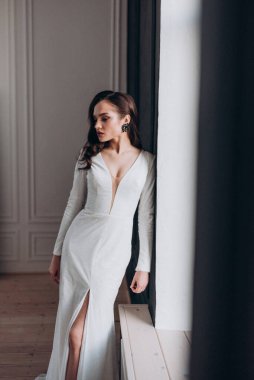 Beyaz parlak gelinlik içinde kahverengi saçlı güzel bir gelin fotoğraf stüdyosunda poz veriyor.