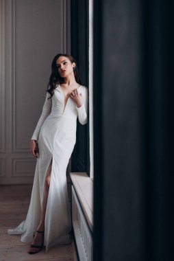 Beyaz parlak gelinlik içinde kahverengi saçlı güzel bir gelin fotoğraf stüdyosunda poz veriyor.