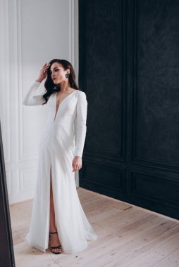 Beyaz parlak gelinlik içinde kahverengi saçlı güzel bir gelin fotoğraf stüdyosunda poz veriyor.