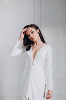 Beyaz parlak gelinlik içinde kahverengi saçlı güzel bir gelin fotoğraf stüdyosunda poz veriyor.