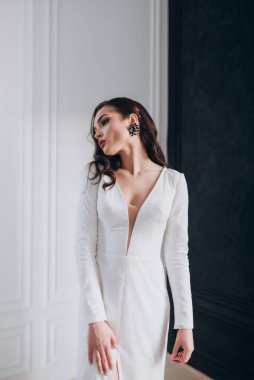 Beyaz parlak gelinlik içinde kahverengi saçlı güzel bir gelin fotoğraf stüdyosunda poz veriyor.