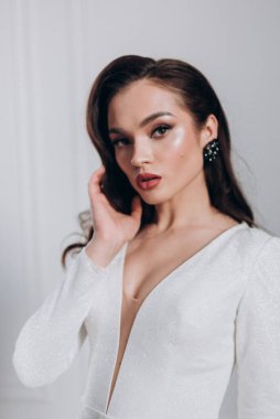 Beyaz parlak gelinlik içinde kahverengi saçlı güzel bir gelin fotoğraf stüdyosunda poz veriyor.