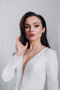 Beyaz parlak gelinlik içinde kahverengi saçlı güzel bir gelin fotoğraf stüdyosunda poz veriyor.