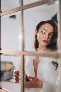 Beyaz parlak gelinlik içinde kahverengi saçlı güzel bir gelin fotoğraf stüdyosunda poz veriyor.