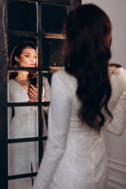 Beyaz parlak gelinlik içinde kahverengi saçlı güzel bir gelin fotoğraf stüdyosunda poz veriyor.