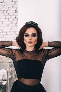 Siyah elbiseli, kahverengi saçlı güzel bir kız fotoğraf stüdyosunda poz veriyor.