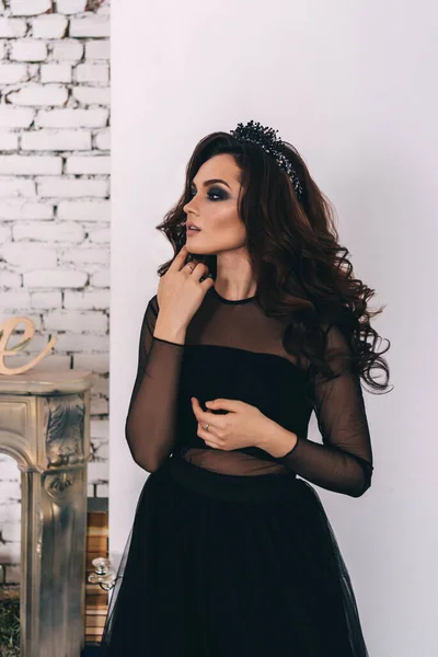 Siyah elbiseli, kahverengi saçlı güzel bir kız fotoğraf stüdyosunda poz veriyor.