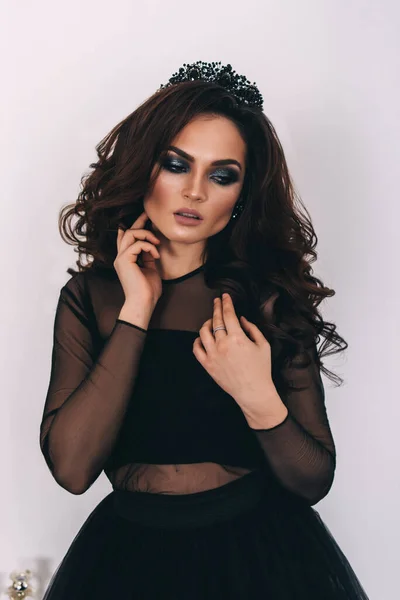 Siyah elbiseli, kahverengi saçlı güzel bir kız fotoğraf stüdyosunda poz veriyor.
