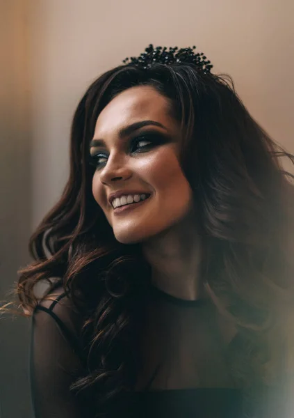 Siyah elbiseli, kahverengi saçlı güzel bir kız fotoğraf stüdyosunda poz veriyor.