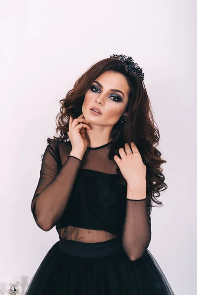 Siyah elbiseli, kahverengi saçlı güzel bir kız fotoğraf stüdyosunda poz veriyor.