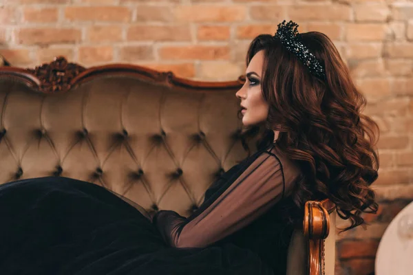 Siyah elbiseli, kahverengi saçlı güzel bir kız fotoğraf stüdyosunda poz veriyor.