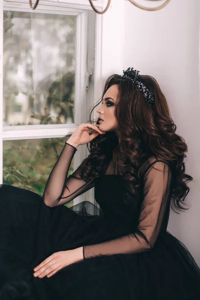 Siyah elbiseli, kahverengi saçlı güzel bir kız fotoğraf stüdyosunda poz veriyor.