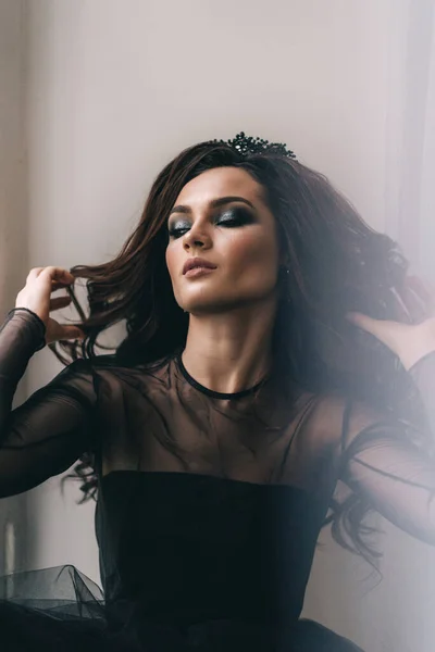 Siyah elbiseli, kahverengi saçlı güzel bir kız fotoğraf stüdyosunda poz veriyor.