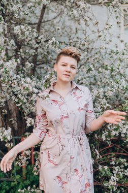 Kısa sarı saçlı bir kız baharda açan beyaz kiraz çiçekleriyle çevrilidir.