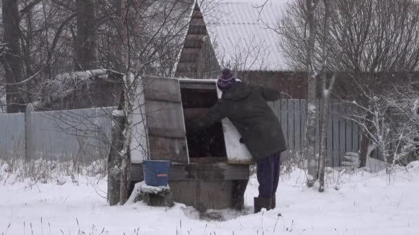 Человек зимой черпает и заливает воду в колодец. прядет ведро с водой . — стоковое видео
