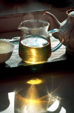 Güneş ışınları yeşil çay dolu bir cam kaseden geçer. Çay tepsisinde çay dolu bir kase var.