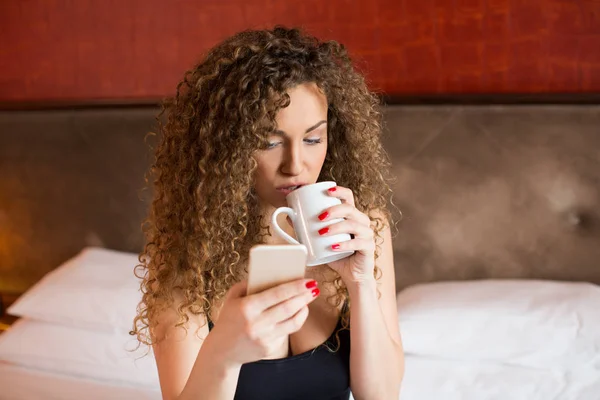 Молодая женщина дома пьет кофе и пишет смс — стоковое фото