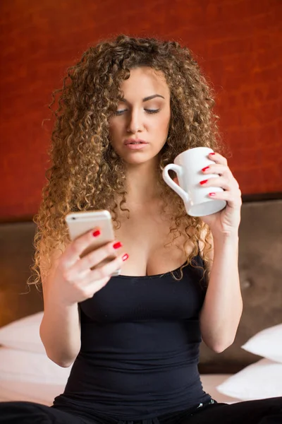 Νεαρή γυναίκα στο σπίτι πίνει καφέ και γραπτών μηνυμάτων — Φωτογραφία Αρχείου
