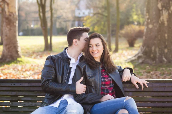 Feliz joven pareja sentada en un banco en el parque — Foto de Stock