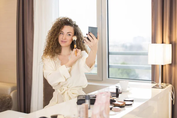 Νεαρή γυναίκα κοιτάζοντας στον καθρέφτη και να βάζει κάποιο μακιγιάζ — Φωτογραφία Αρχείου