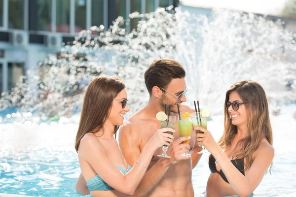 Hombre entre dos mujeres en la piscina tomando bebidas — Foto de Stock
