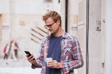 adam elinde kahve fincanı ve telefon, şehir çevre