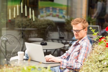 Kafede oturan ve dizüstü bilgisayarda çalışan yakışıklı adam