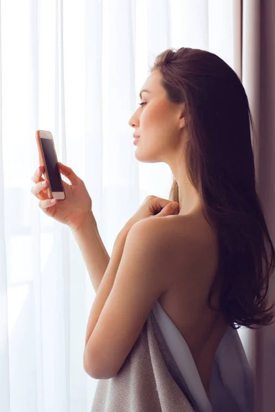 Mooie vrouw met mobiele telefoon door het venster — Stockfoto