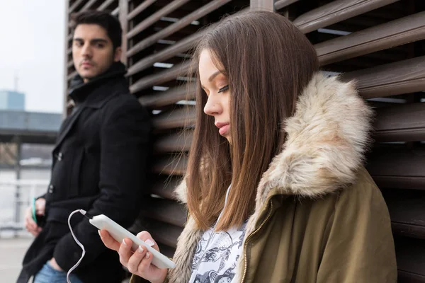 Mujer joven mirando el teléfono móvil, hombre celoso en el backgrou — Foto de Stock