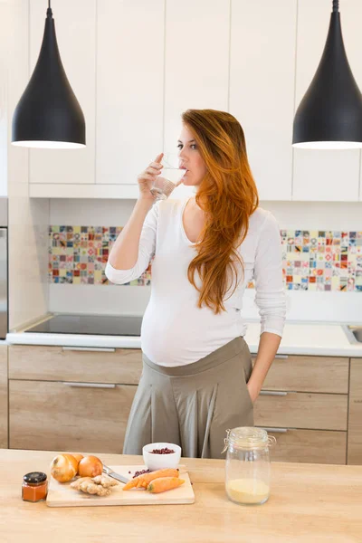 Těhotná žena, příprava jídla, zeleniny a pít vodu — Stock fotografie