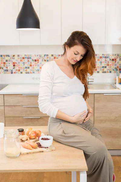 Pregnant woman preparing meal, vegetables, and looking her belly — Stock Photo, Image