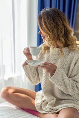 Çekici genç bir kadın otel odasında kahve içiyor.