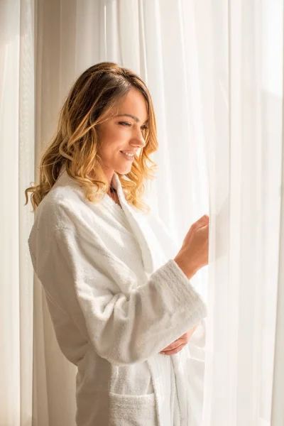 Aantrekkelijke jonge vrouw kijkend door het raam in hotelkamer — Stockfoto