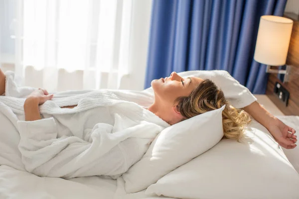 Mooie vrouw in badjas ontspannen in hotel bed — Stockfoto