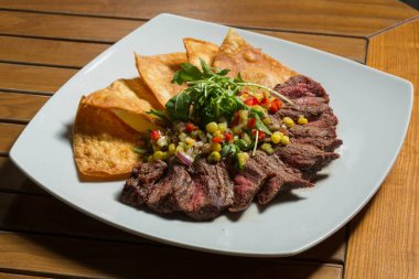 Nacho ve sebzeli baharatlı biftek beyaz tabakta servis edilir.