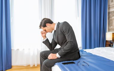 Otel yatağında oturan sinirli işadamı