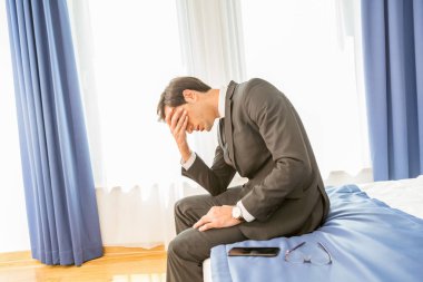 Hüsrana uğramış iş adamı otel yatağında oturmuş elini tutuyor.