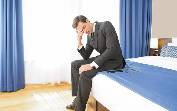 Απογοητευμένος επιχειρηματίας κάθεται στο κρεβάτι του ξενοδοχείου — Φωτογραφία Αρχείου