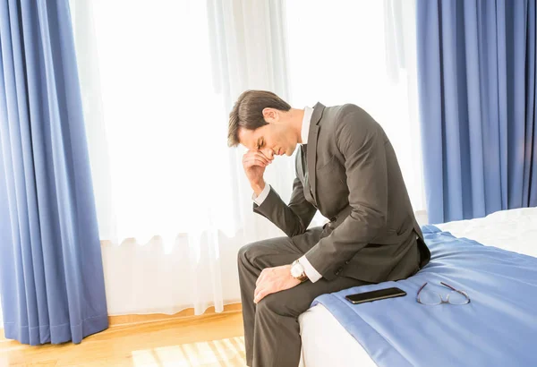 Gefrustreerde zakenman die op het hotelbed zit en zijn hand vasthoudt — Stockfoto