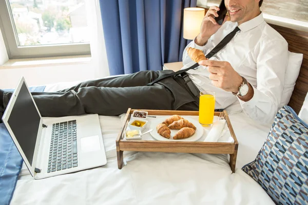 Empresário tomando café da manhã em uma cama de hotel — Fotografia de Stock